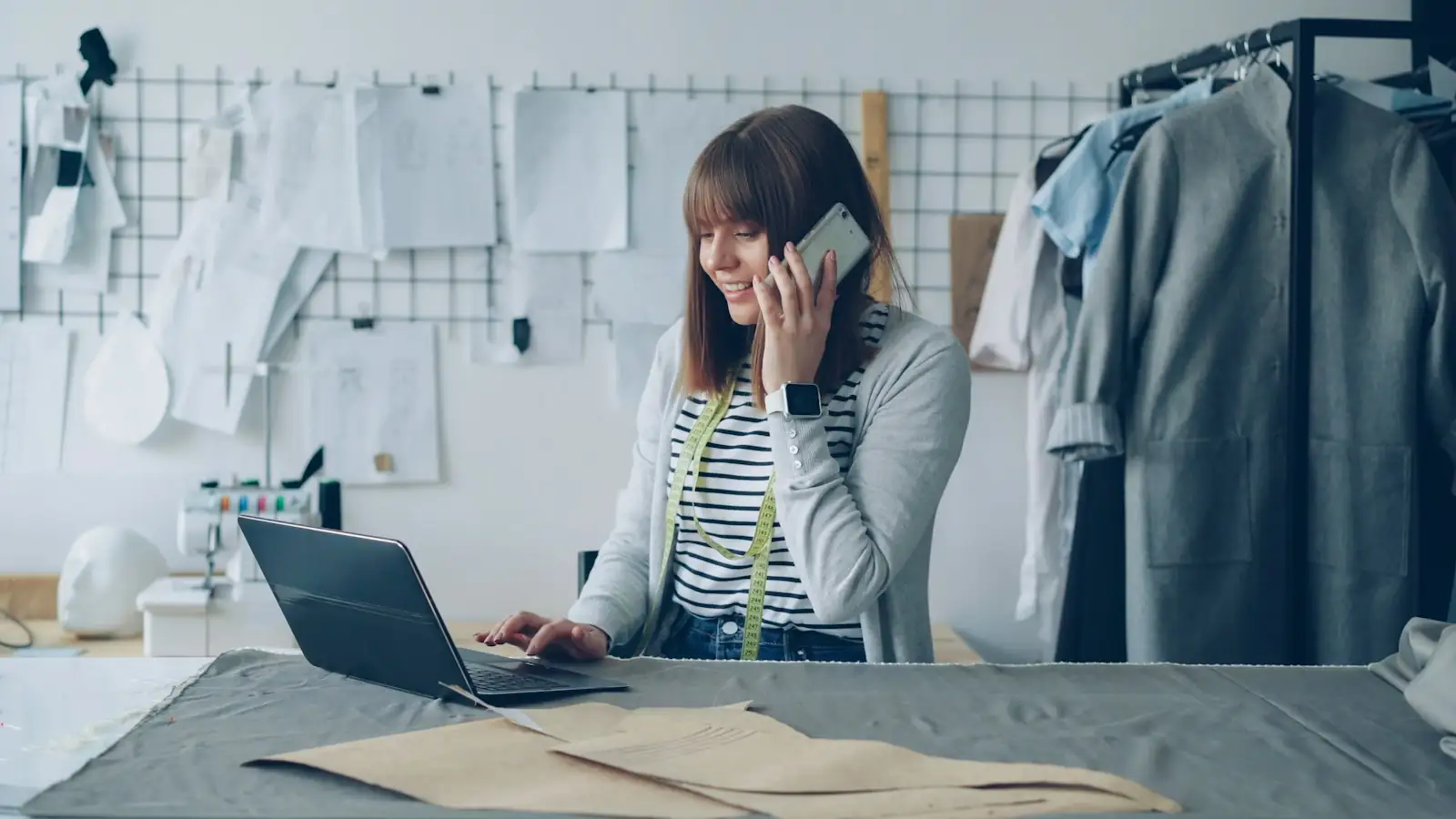 Business owner on the phone working through paperwork at her laptop